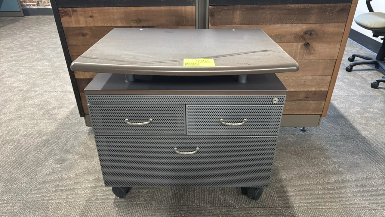 Portable printer station. Features an elevated laminate top shelf on riser posts, perforated metal cabinet with (2) upper drawers and (1) lower storag