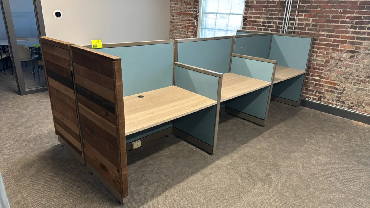 6-cubicle modular workspace system. Features blue fabric divider panels, light woodgrain laminate desktop surfaces with cable grommets, metal trim, an