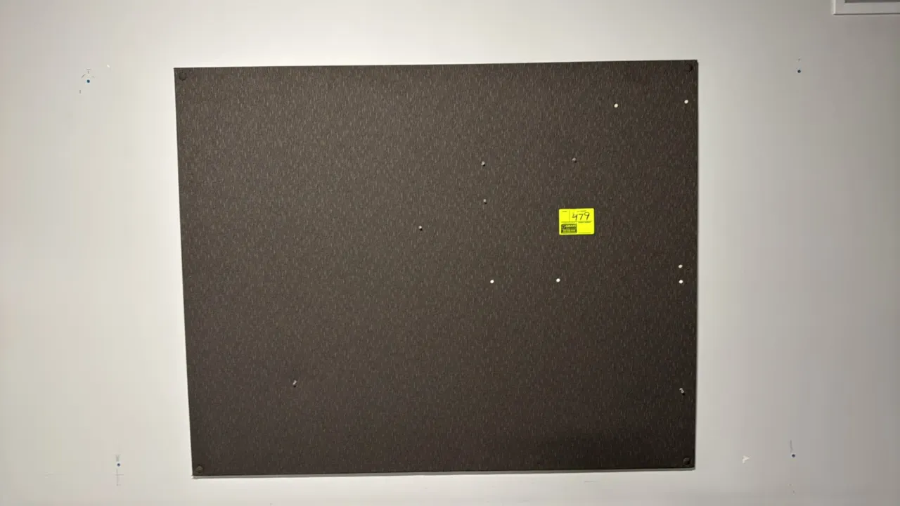 Fabric-covered cork bulletin board. Features dark gray textured fabric facing. Dimensions: 6' x 4'. Wall-mounted.