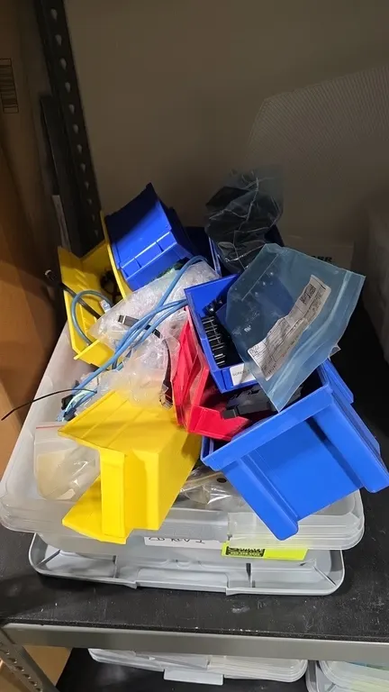 Hefty clear plastic storage tote with assorted parts bins and components. Includes blue, yellow, and red plastic storage bins, cables, and miscellaneo