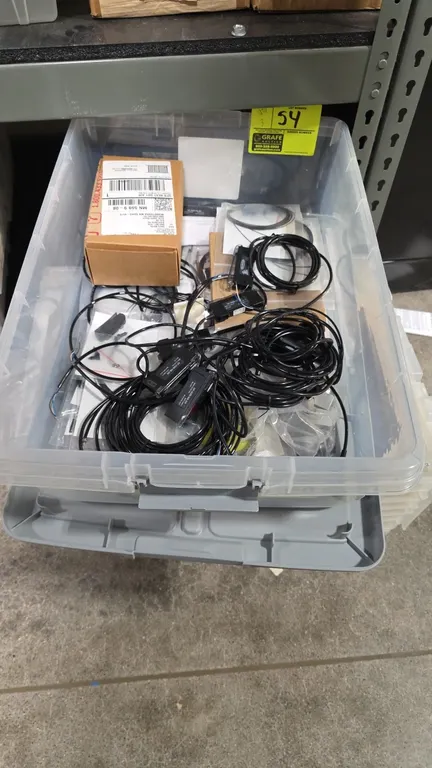 Plastic storage totes with assorted components. Contents include Banner sensors with cabling, wiring harnesses, printed circuit boards, and related el