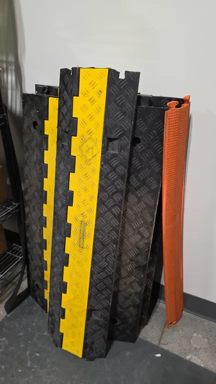 Rubber cable and hose protectors. Features heavy-duty rubber construction with textured diamond-plate traction surface, hinged yellow safety lids, and