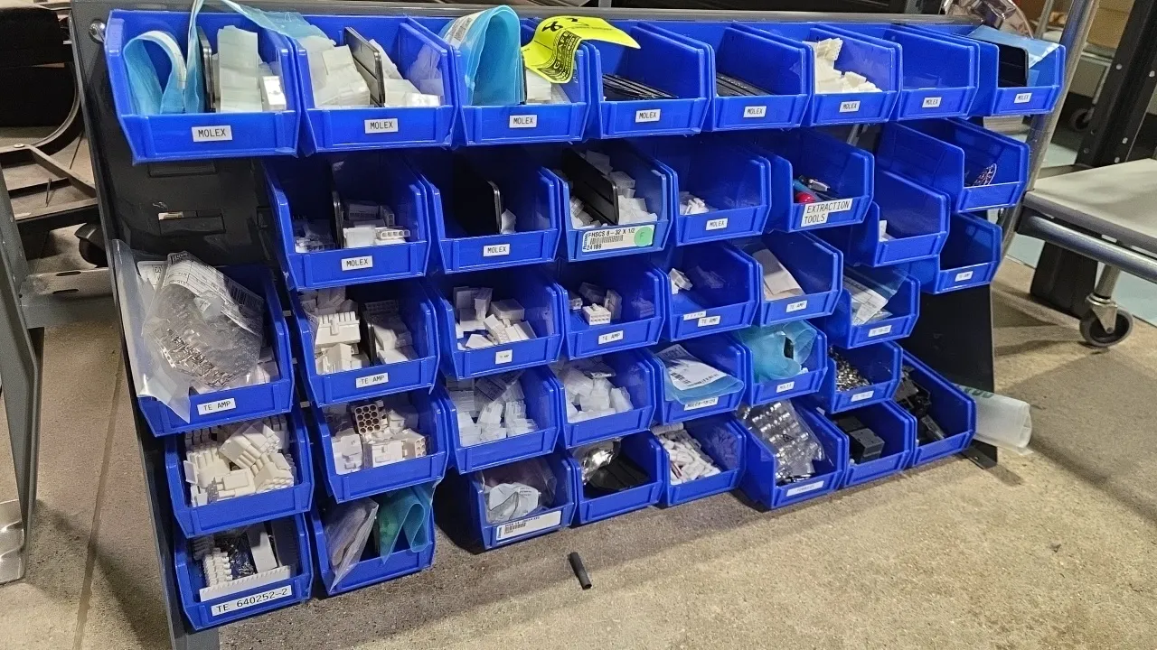Metal counter frame organizer stand. Features a louvered metal frame rack with multi-tier blue poly hanging bins and assorted contents, including Mole