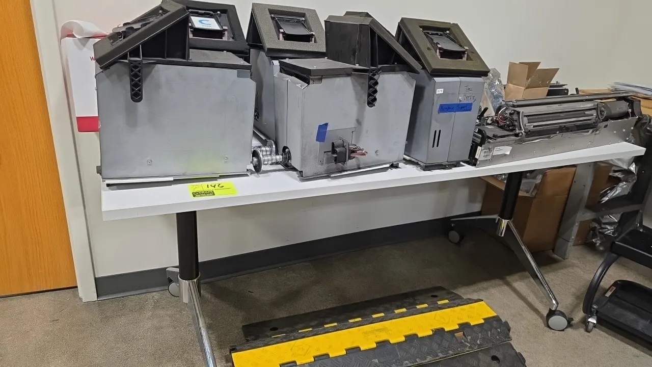 Portable table with assorted printer parts. Features a white laminate top and metal frame mounted on casters. Includes assorted printer component asse