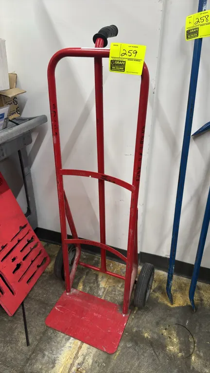 Metal 2-wheel hand truck. Features a red tubular steel frame, single center grip handle, and solid wheels.