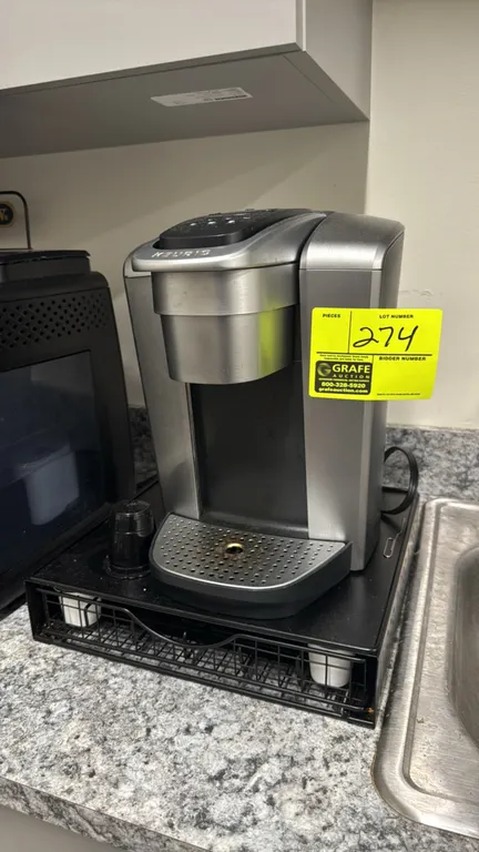 Keurig single-serve coffee maker. Features brushed silver and black finish, digital top controls, removable drip tray, water reservoir, and a pull-out