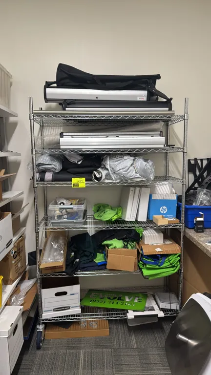 Chrome 6-tier portable wire shelving rack with contents. Includes assorted Evolve logo apparel and merchandise, aluminum retractable banner stands, an