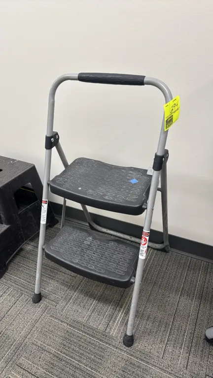 Werner StepRight 2-step folding step stool. Features a tubular metal frame, molded textured steps, padded hand grip, and folding mechanism with lockin