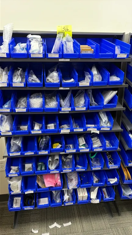 Multi-tier parts storage rack with blue plastic bins and assorted contents. Includes various relays, copper fittings, conductors, fuses, and hardware.