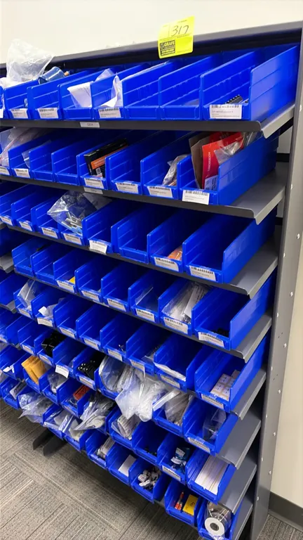 Metal parts bin rack with blue plastic storage bins and assorted contents. Includes filter driers, belts, nuts, bolts, brass fittings, barrier strips,