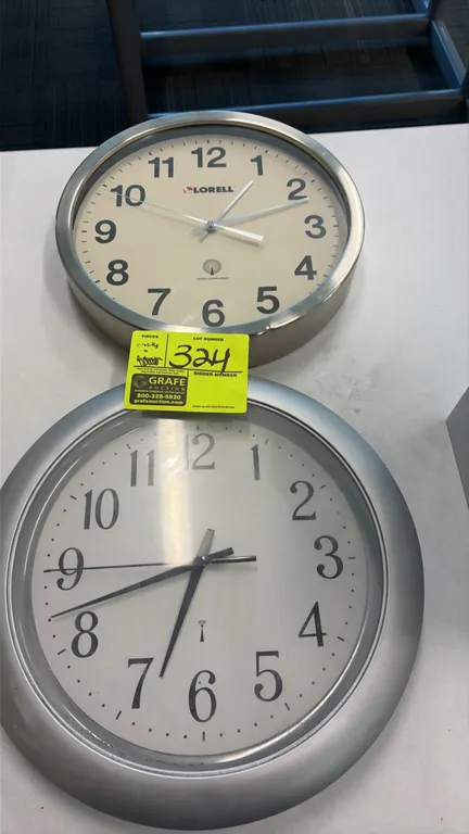 Lorell and unbranded radio-controlled wall clocks. Lot includes (1) Lorell clock with brushed metal bezel and (1) wall clock with silver-tone molded b