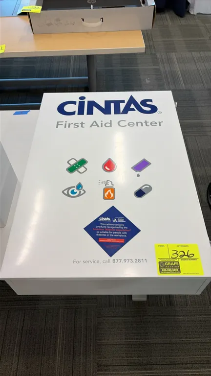 Cintas First Aid Center first aid cabinet. Features white metal construction, hinged door with interior pocket organizer, multi-tier shelving, and ass