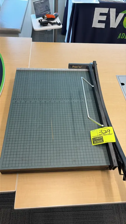 Premier guillotine paper cutter. Features alignment grid with ruler markings, guillotine cutting blade, and wire safety guardrail.