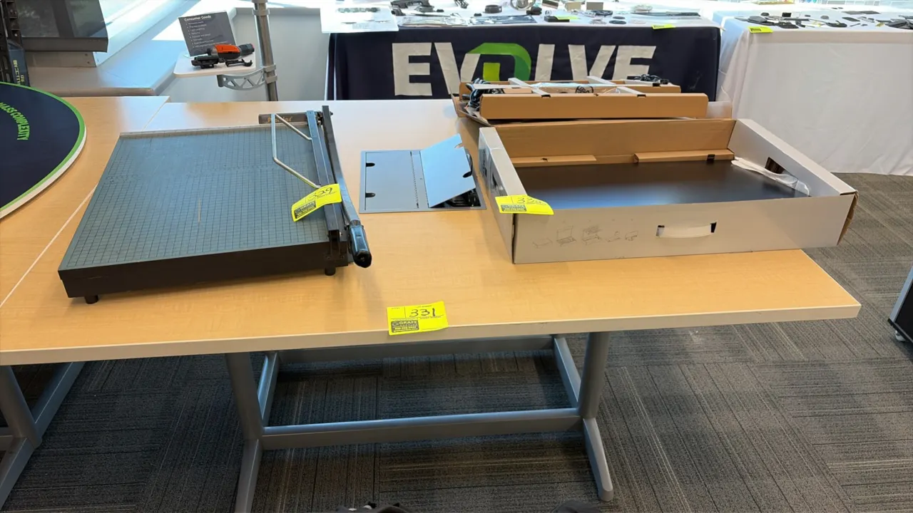 Wood laminate workstation table. Features an integrated flip-top electrical power module. Mounted on a gray metal frame with crossbar. 60" x 48". Cont