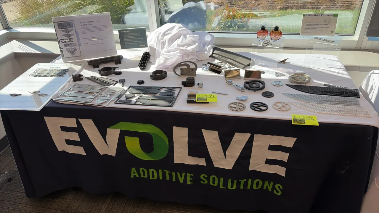 Evolve Additive Solutions trade show booth display automotive sample parts and branded table cover. Includes 3D printed automotive components, decorat