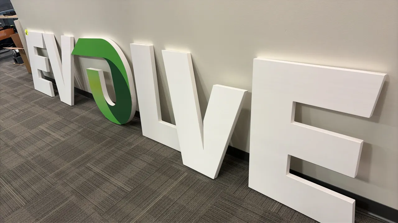 Dimensional individual wood letters for "EVOLVE" wall sign. Features painted white and green finish with stylized logo element.