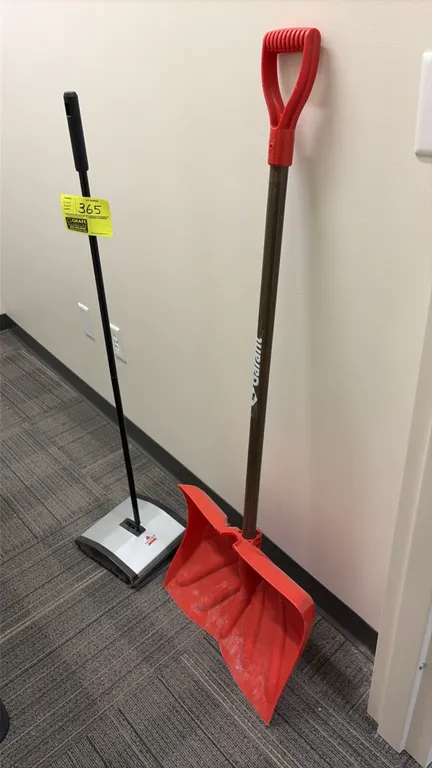Bissell manual floor sweeper and Garant snow shovel. Sweeper features a low-profile base and metal handle with grip. Shovel features a red poly blade,