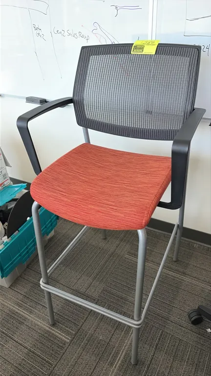 High-top office chair stool. Features black mesh back, orange fabric upholstered seat, fixed armrests, and integrated footrest. Mounted on silver-tone