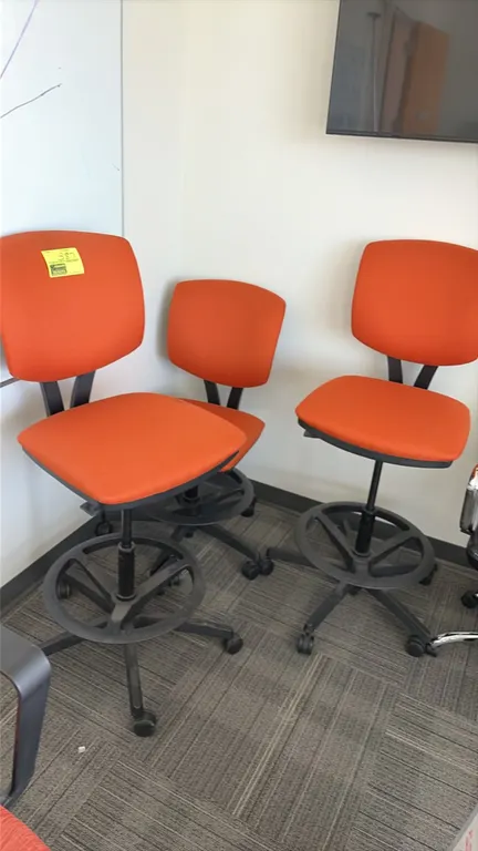 Drafting chairs. Features orange fabric upholstery, armless design, and integrated foot rings. Mounted on 5-star bases with rolling casters.