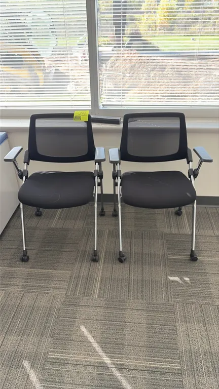 Flip-up nesting office chairs. Features black mesh backrest, black upholstered flip-up seat, fixed armrests, and chrome frame. Mounted on casters.