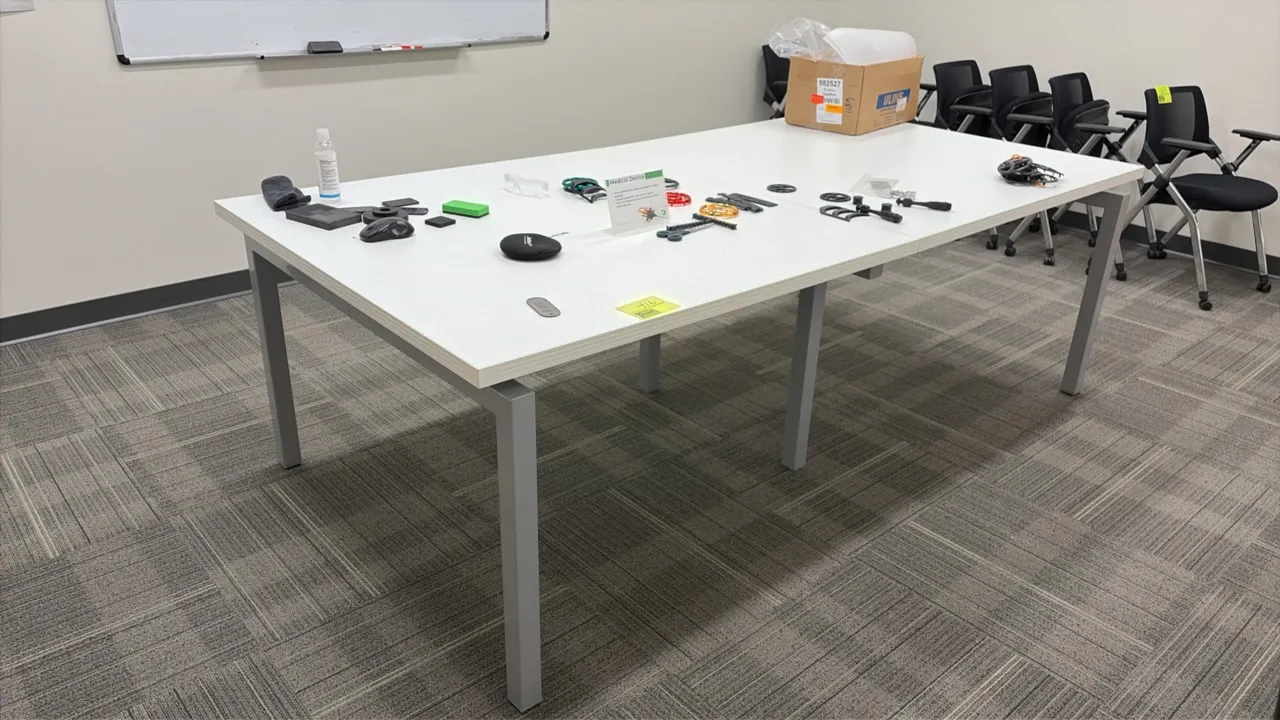 Wood laminate conference table. Features a white laminate top. Mounted on a gray metal frame. 94 1/2" x 48". Includes assorted parts. Chairs in backgr