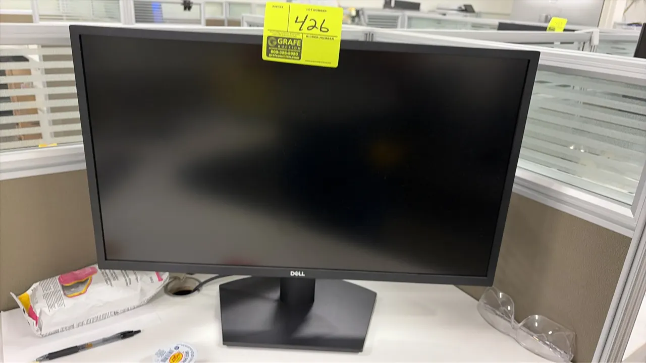 Dell 24" computer monitor. Features a widescreen display with a matte black finish. Mounted on matching desktop stand. Desk accessories and items in b