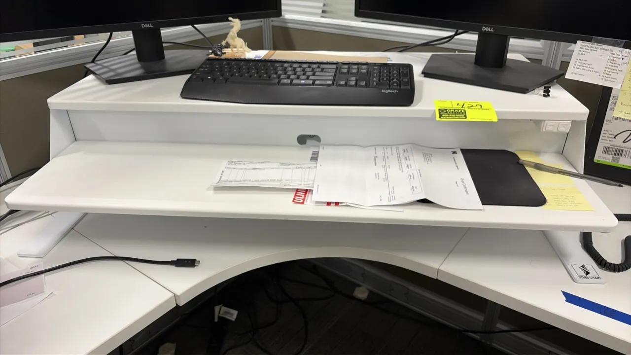 Stand Steady electric standing desk converter. Features a two-tier white laminate construction with an upper monitor platform, lower keyboard tray, ca