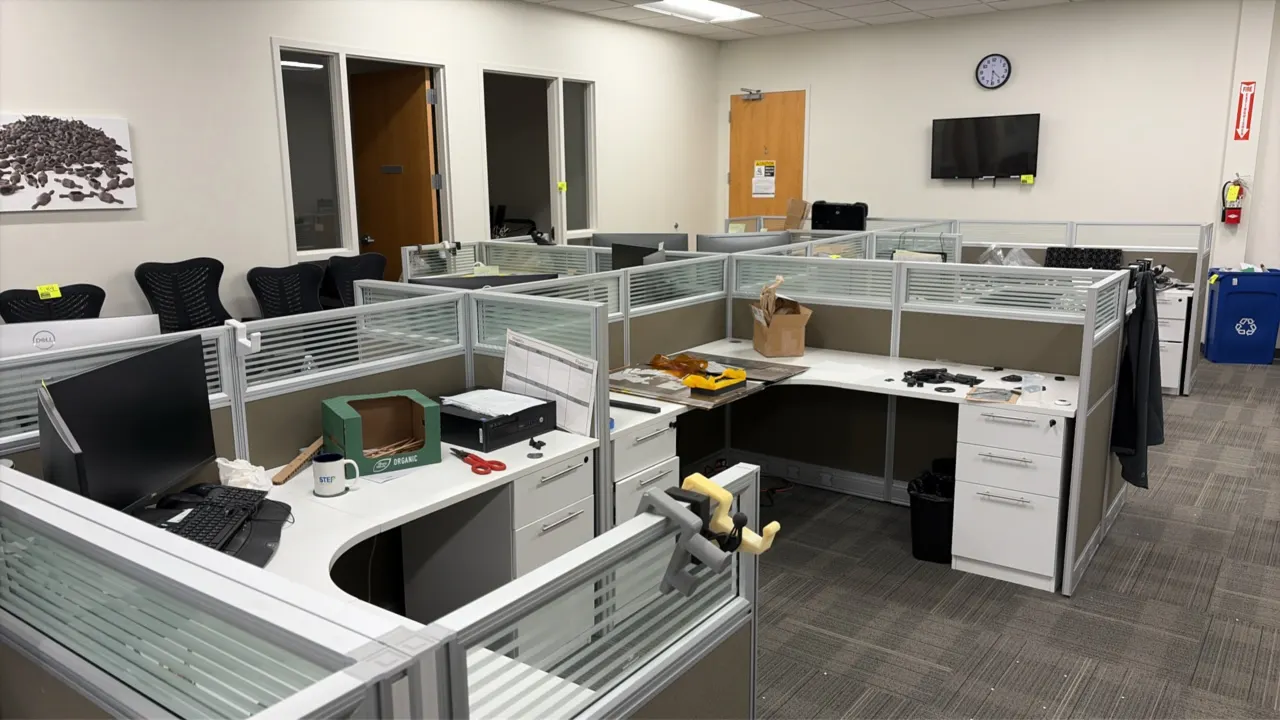 12-workstation cubicle system. Features fabric acoustic partition panels with frosted glass toppers, white laminate work surfaces, and integrated 3-dr