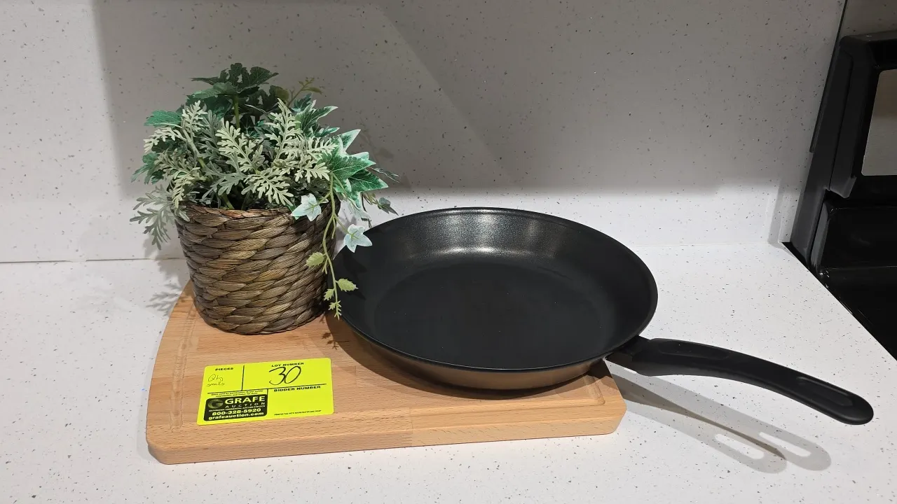 Assorted kitchen smallwares and decor. Includes non-stick frying pan, wooden cutting board, artificial plant in woven basket planter, white embossed c