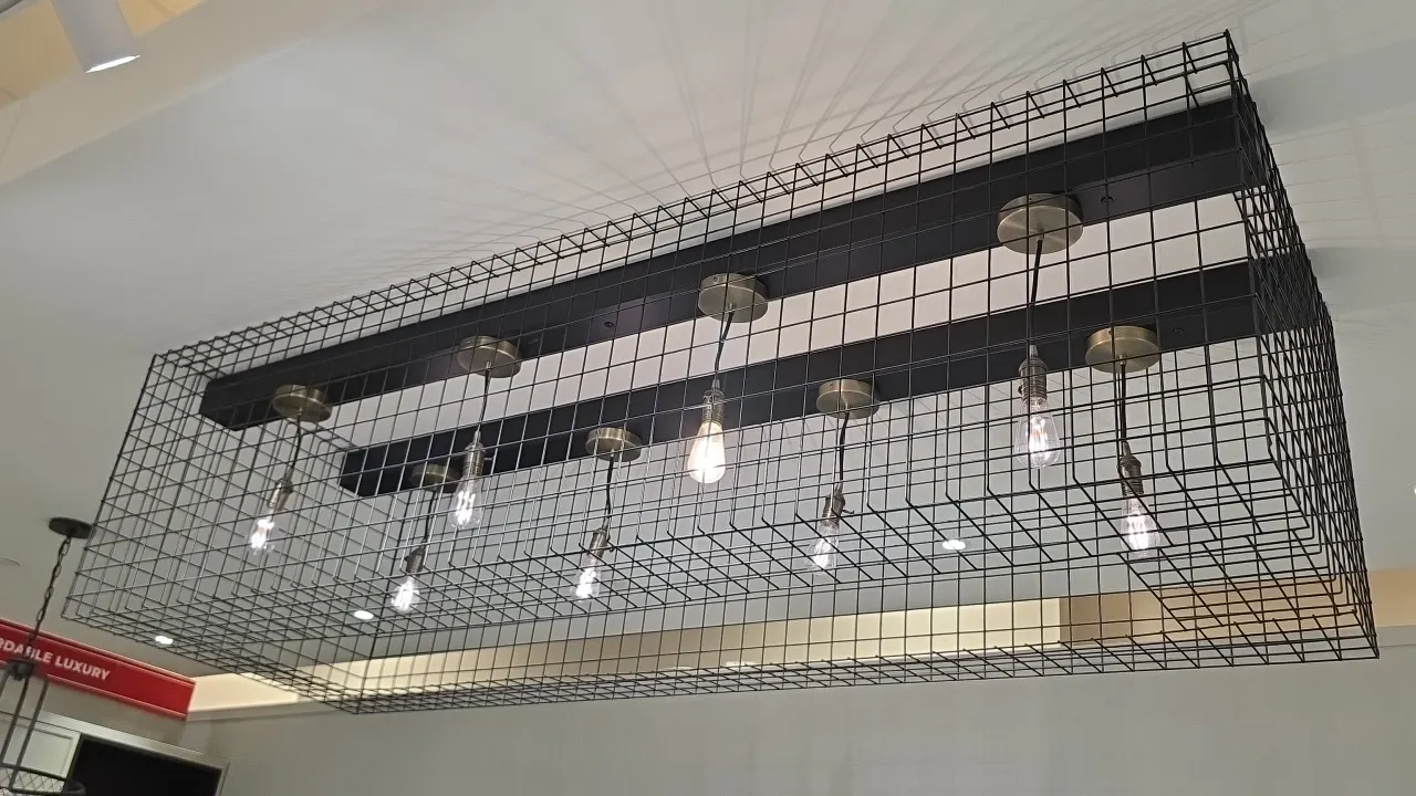 Wire mesh over-island pendant light fixture. Features black metal dual-rail frame, wire mesh cage design, and (8) pendant lights with brass-tone socke