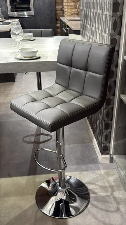 Adjustable-height pedestal barstools. Features gray tufted upholstery, integrated footrests, and pneumatic height adjustment. Mounted on round chrome