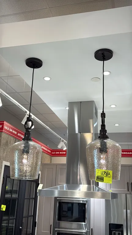 Hanging glass pendant lights. Features textured glass shades, dark bronze-finished hardware with decorative ring accents, adjustable hanging cords, an