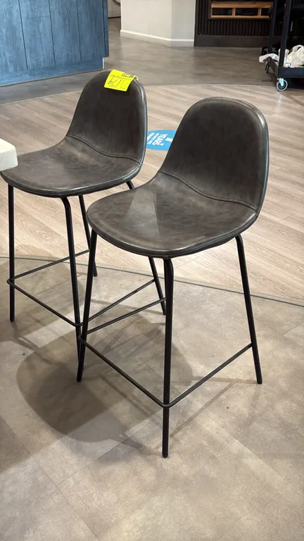 Grey padded counter stools. Features grey upholstered seats and black metal frames with integrated footrests. 24" seat height.