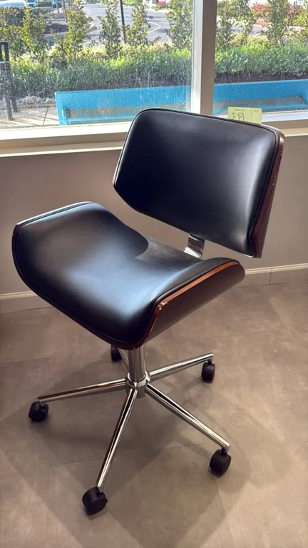 Mid-century modern style rolling desk chair. Features a bentwood shell with woodgrain finish, armless design, and black padded seat and back. Mounted