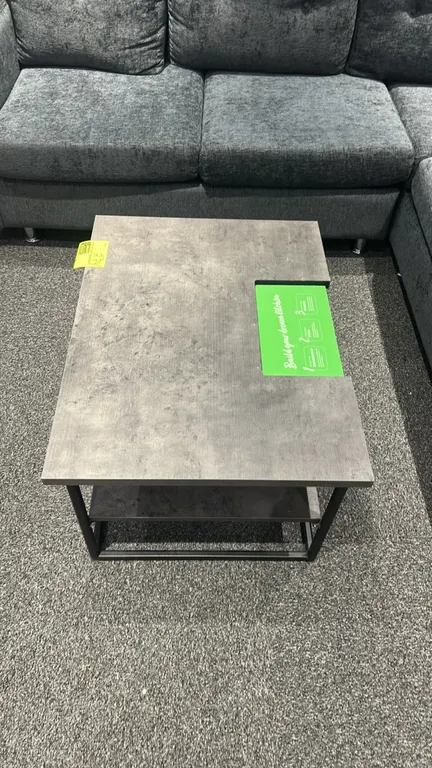 Two-tier laminate table. Features gray concrete-look laminate top with display cut-out section and lower shelf. 32" x 24". Mounted on a black metal fr