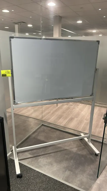 Mobile whiteboard. Features an aluminum frame and integrated marker tray. 4'W. Mounted on a painted metal easel stand with casters.