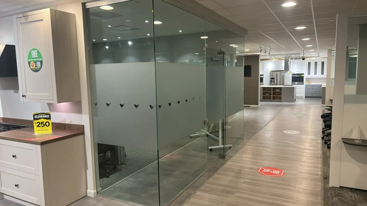 Architectural glass office partition enclosure. Features frameless tempered glass panels with frosted privacy film, bird silhouette manifestation grap