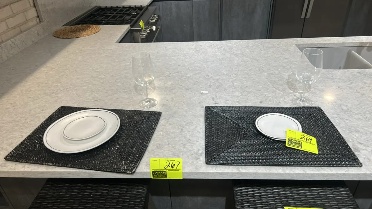 Assorted kitchen smallwares and table setting accessories. Includes woven placemats, white ceramic plates, stemmed wine glasses, round woven trivet, a
