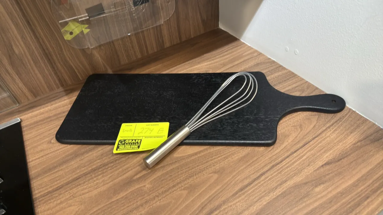 Assorted kitchen smallwares and glassware. Includes black paddle-style serving board, stainless steel wire whisk, (2) stemmed champagne flutes, and (4