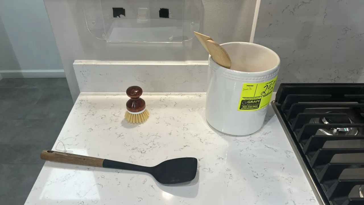 Assorted kitchen smallwares and decor. Includes wooden serving tray, decorative metal pitcher, artificial potted plant, glassware, ceramic utensil cro