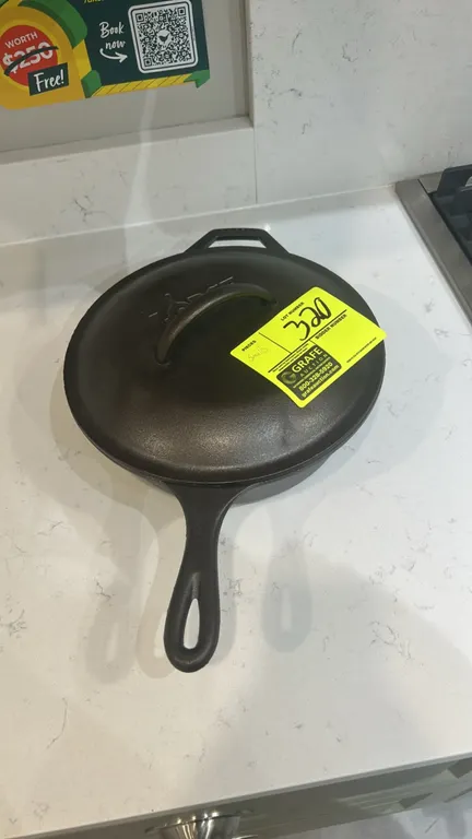 Assorted kitchen smallwares and decor. Includes Lodge cast iron deep skillet with lid, metal wire dish drying rack with wood handles, wood cutting boa