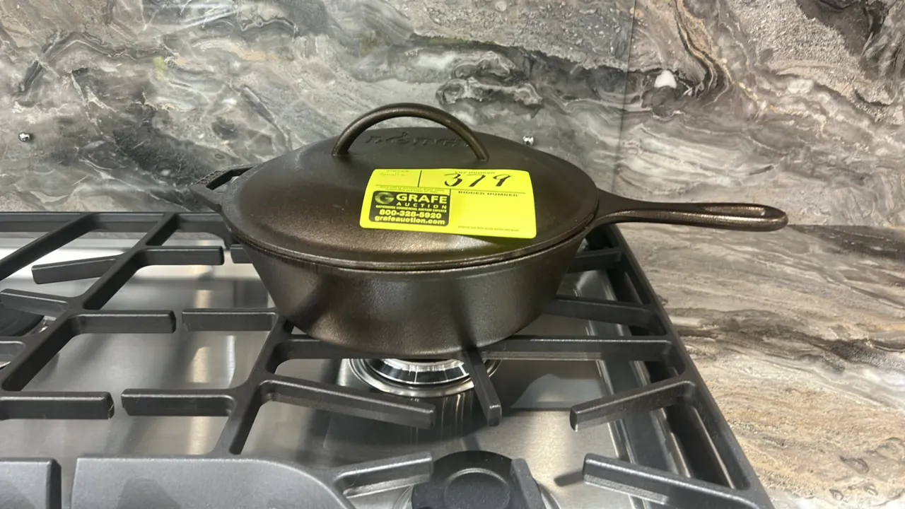 Assorted smallwares. Includes Lodge cast iron deep skillet with matching lid and helper handle, and an artificial potted plant in a white bowl. Range