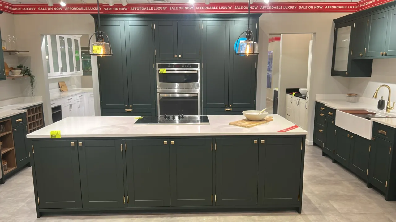 Infinity Plus kitchen cabinetry and island suite. Features dark green laminate cabinets with brass-tone hardware, white quartz countertops, glass-door