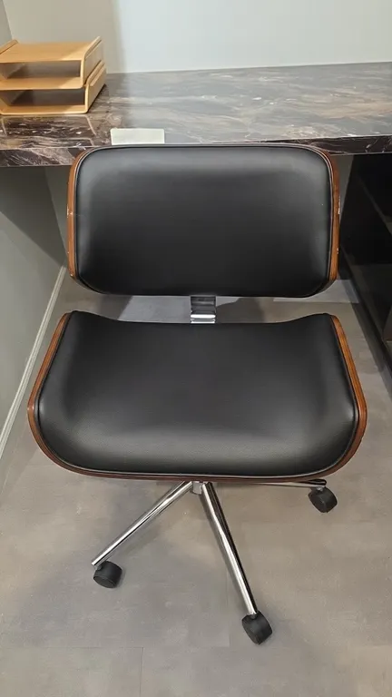 Adjustable office chair. Features a bentwood laminate shell with walnut finish, black faux leather upholstered seat and back, armless design, and pneu