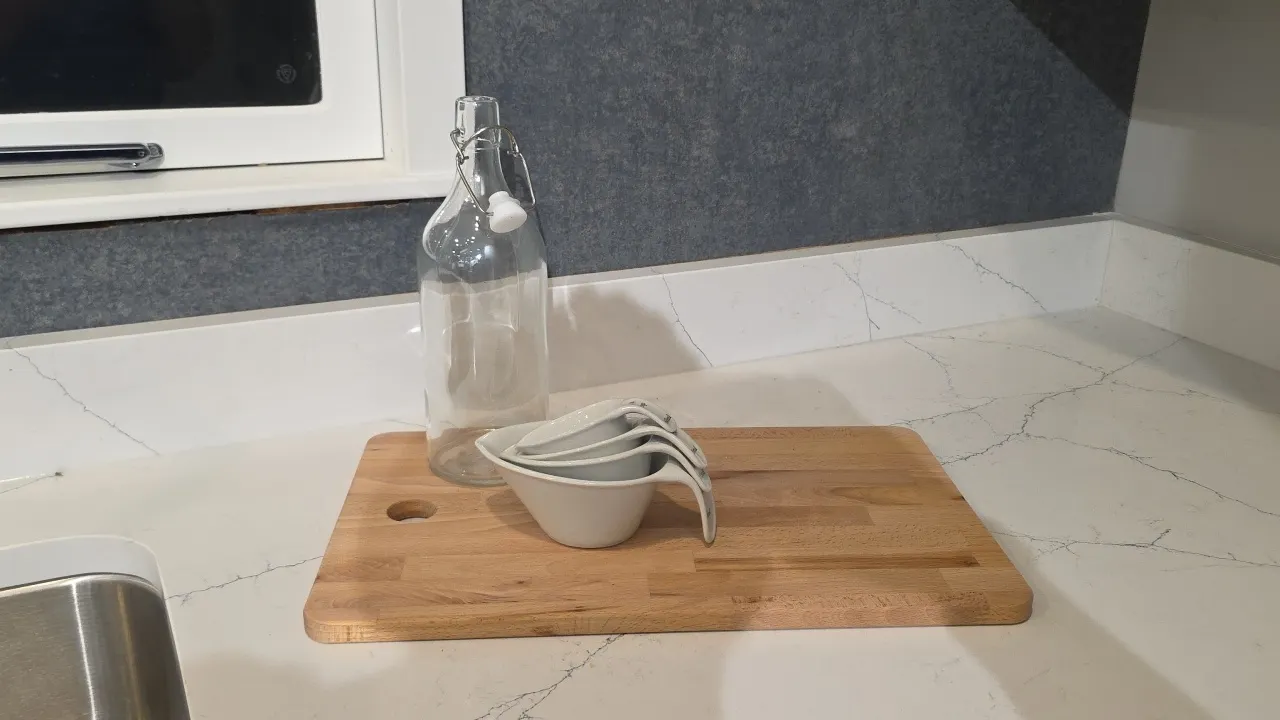 Assorted kitchen smallwares and decor. Includes ceramic utensil crock with utensils, wooden cutting boards, swing-top glass bottle, ceramic measuring