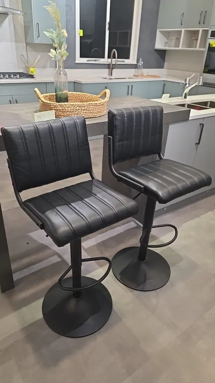 Adjustable barstools. Features black faux leather channel-tufted upholstery, integrated footrests, and height adjustment levers. 30" seat height, 42"H