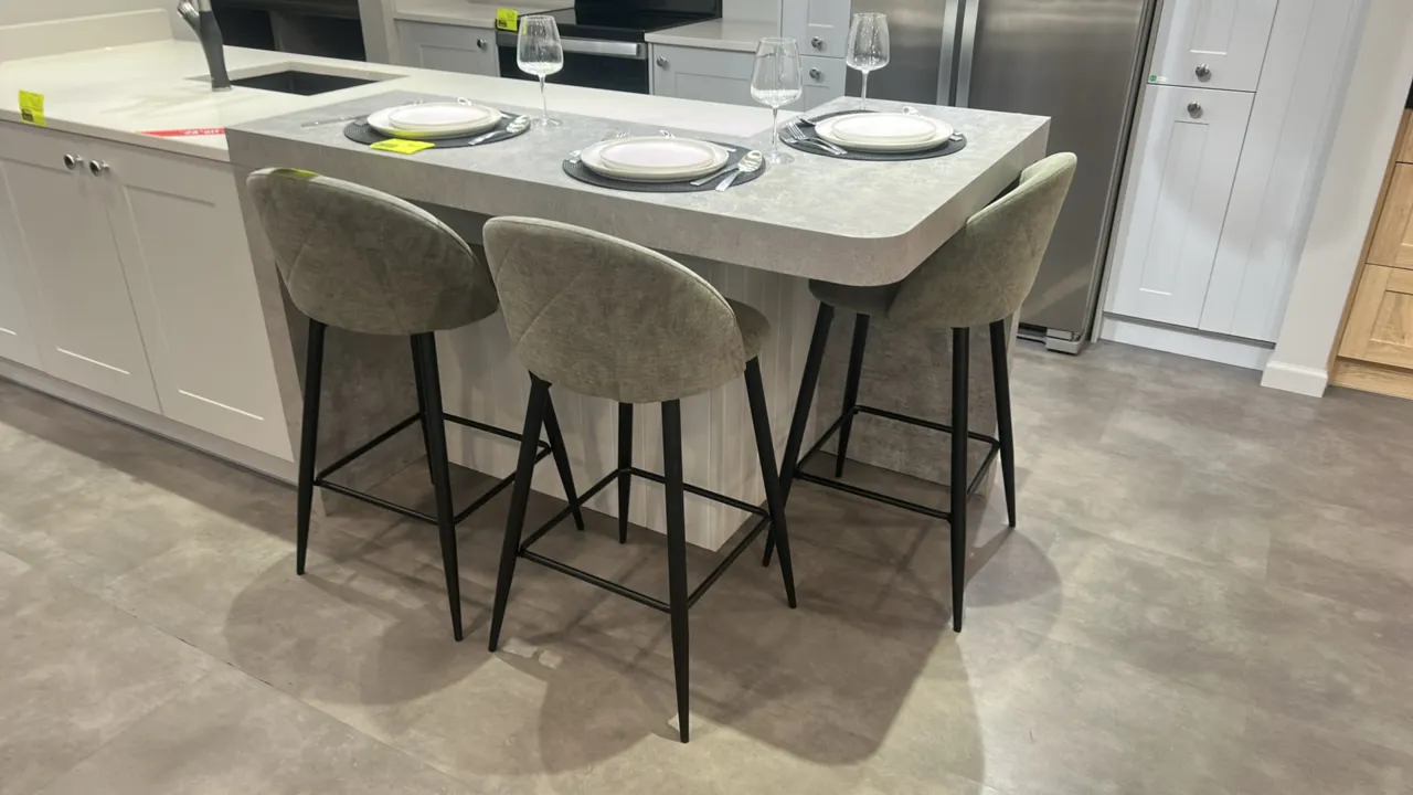 Cushioned barstools. Features textured gray-green fabric upholstery with quilted backrests. Mounted on black metal tapered four-leg bases with integra