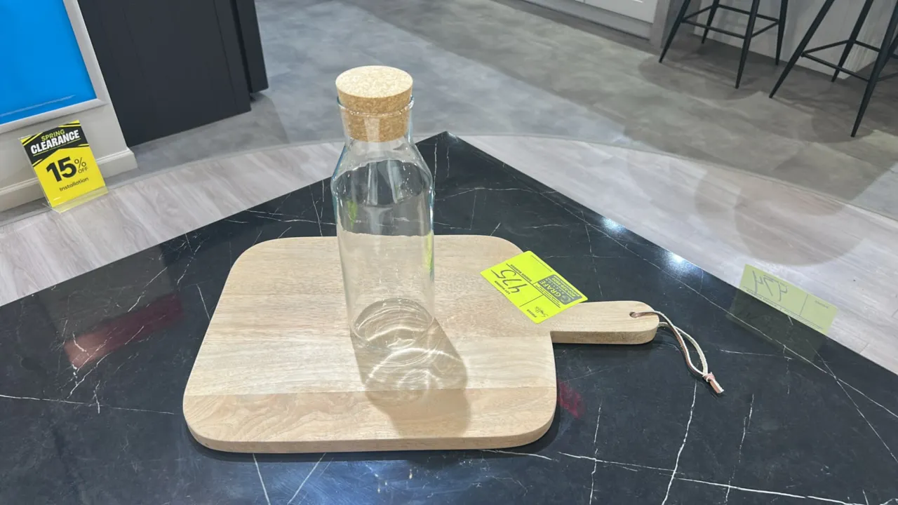 Assorted kitchen smallwares and decor. Includes wooden cutting board with handle, glass bottle with cork stopper, glass canisters with lids, ceramic p