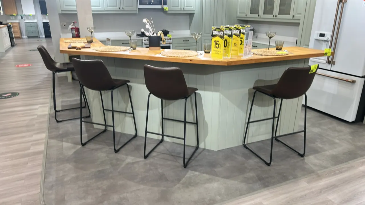 Cushioned barstools. Features brown faux leather cushioned seats with decorative perimeter stitching and integrated footrests. Mounted on black metal