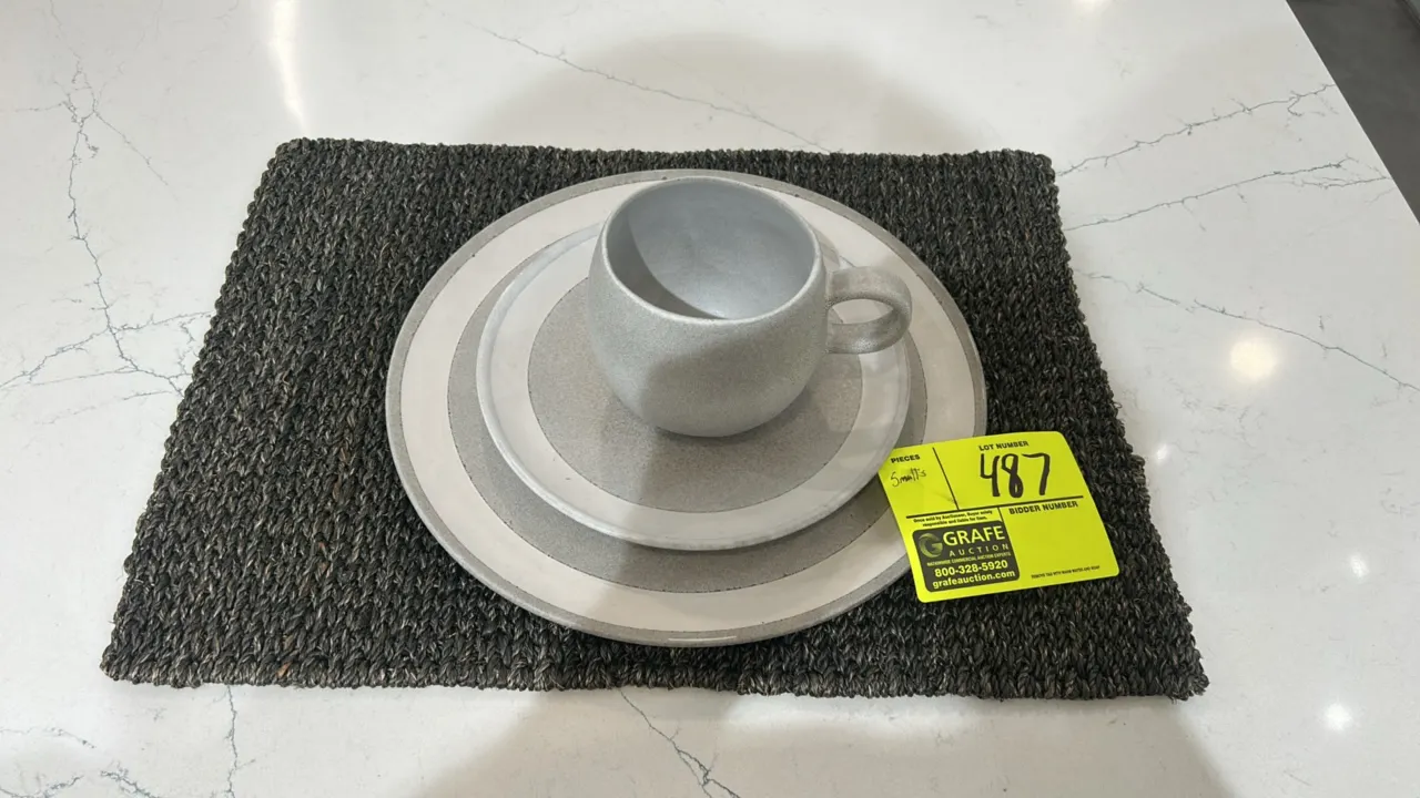 Assorted tabletop and kitchen smallwares. Includes wooden cutting board, glass French press coffee maker, ceramic dinnerware plates, mugs, and woven p
